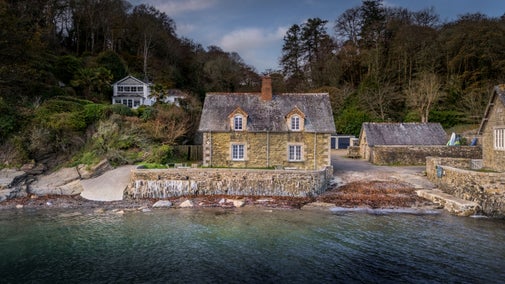 An aerial view of semi-detached cottages, Durgan Beach Cottage (on the right) and Durgan Quay Cottage (on the left) at high tide, Cornwall